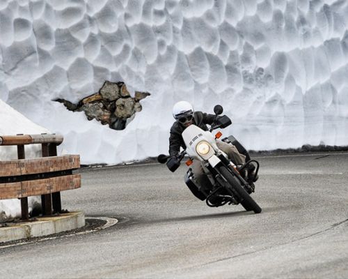 <p><span style="font-weight: 400;">El invierno puede traer condiciones muy duras. Nieve, viento, granizo y en el mejor de los casos, frío intenso es lo que nos espera a muchos motoristas si vivimos en zonas donde esta época del año nos hace sufrir todo su rigor. </span><span style="font-weight: 400;">Para conducir la moto sobre nieve, primero debemos tener en cuenta un par de factores que pueden ser determinantes. Es muy diferente que la situación nos sorprenda, por una mala previsión puntual y otra muy distinta es que afrontemos una ruta o desplazamiento sabiendo que nos podemos encontrar con una climatología adversa.</span></p> <p><span style="font-weight: 400;">Hay concentraciones invernales que por la época del año que se celebran y la situación geográfica lo realmente sorprendente sería que hubiera un tiempo más amable que lo normal.</span></p> <p><span style="font-weight: 400;">Una de las más conocidas por las extremas condiciones es la </span><a href="https://bvdm.de/aktivitaeten-und-fahrspass/elefantentreffen/"><span style="font-weight: 400;">Elefantentreffen</span></a> <span style="font-weight: 400;">(quedada de elefantes en español) que se celebra en Alemania, cerca de la frontera con la República Checa, en los bosques de Baviera. La temperatura puede rondar -20 ºC. Por consiguiente quienes tienen pensado asistir ya lo hacen sobradamente preparados para afrontar esas condiciones.</span></p> <p><span style="font-weight: 400;">Lo principal a la hora de enfrentarse ante una situación de nieve en la carretera es conservar la calma y el sentido común. Trataremos de seguir la huella que dejan en el asfalto los vehículos que nos preceden. Debemos buscar el máximo contacto con la superficie limpia de nieve, no hacer movimientos bruscos, anticiparnos a posibles frenazos conservando la distancia y tocando muy ligeramente el freno para evitar que se formen capas de hielo en las pastillas. </span></p> <p><span style="font-weight: 400;">En estas condiciones el proceso de frenado es tratar de estabilizar la dirección de la moto con el freno trasero, dando toques al mismo y a su vez ejecutar de manera gradual el delantero. Aquí hay ventaja para las motos dotadas de <a href="https://www.ngbrakes.com/blog/2019/11/08/como-frenar-si-tu-moto-tiene-abs/" target="_blank" rel="noopener noreferrer">ABS</a> pero igualmente no es la solución definitiva.</span></p> <p><span style="font-weight: 400;">Se aconseja llevar una relación de marchas lo más larga posible, así no tendremos la sensación de que la rueda va traccionando en falso todo el tiempo con la moto sobre nieve.</span></p> <p><span style="font-weight: 400;">Además tu postura debe ser relajada, atento por si tenemos que apoyar los pies y controlando la conducción desde el manillar y no tanto con el cuerpo. Los movimientos corporales pronunciados tienden apartarse del eje de equilibrio y se transmiten directamente sobre la moto.</span></p> <p><span style="font-weight: 400;">La atención debe ser máxima, evitando zonas sombrías muy propicias a formar placas de hielo o extremando precauciones si han esparcido sal.</span></p> <p><span style="font-weight: 400;">Hay pequeños trucos por si la cosa se pone realmente fea y no tenemos neumáticos adecuados, por ejemplo poner bridas de plástico alrededor de la goma. Otra fórmula es hacer lo mismo que lo anterior pero con una cuerda o con las cinchas de sujeción del equipaje, incluso con el cinturón de tus pantalones.</span></p> <p><span style="font-weight: 400;">Esperamos que no tengas que llegar a tal extremo pero sobre todo recuerda, si vas con la moto sobre nieve te paras en el primer refugio que encuentres y a esperar que mejoren las condiciones o te auxilien. Suerte y prevención.</span></p>
